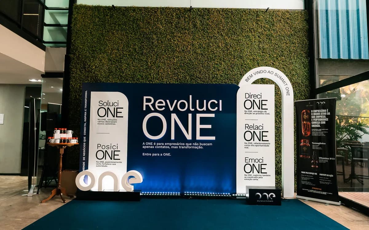 Espaço da ONE na GT House, com parede verde e painel do Summit ONE